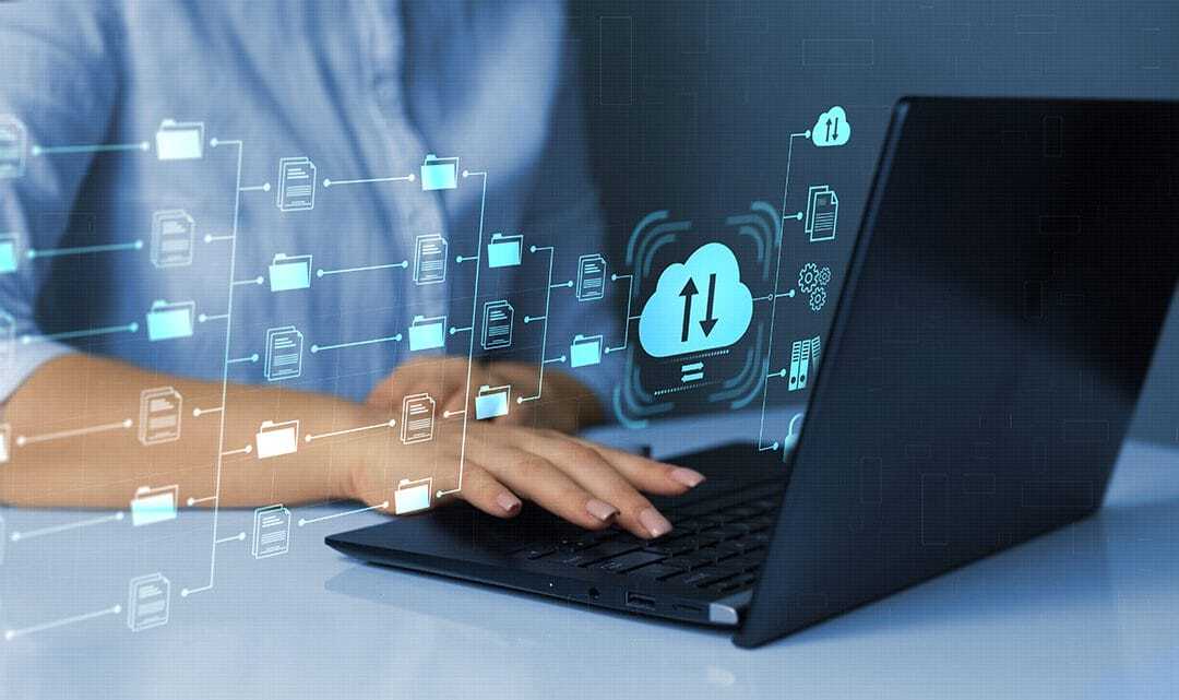 A person using a laptop with digital icons of folders and a cloud, symbolizing cloud computing and data transfer, appearing in front of the screen.