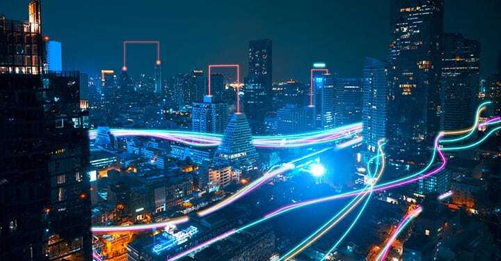 A vibrant cityscape at night with illuminated skyscrapers and colorful light trails weaving through the streets, representing fast digital or data connections in an urban environment.